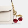 Bolso con el Cherry Bag Charm de Coach, con diseño de cerezas y estilo femenino