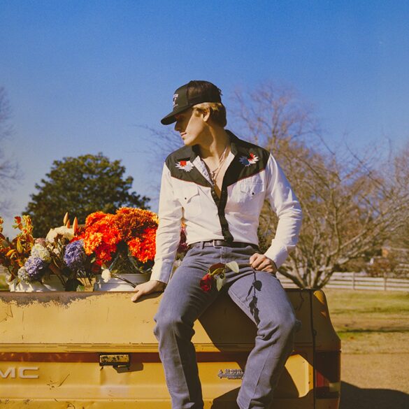 Hudson Westbrook sentado en una cerca, arboles y flores alrededor