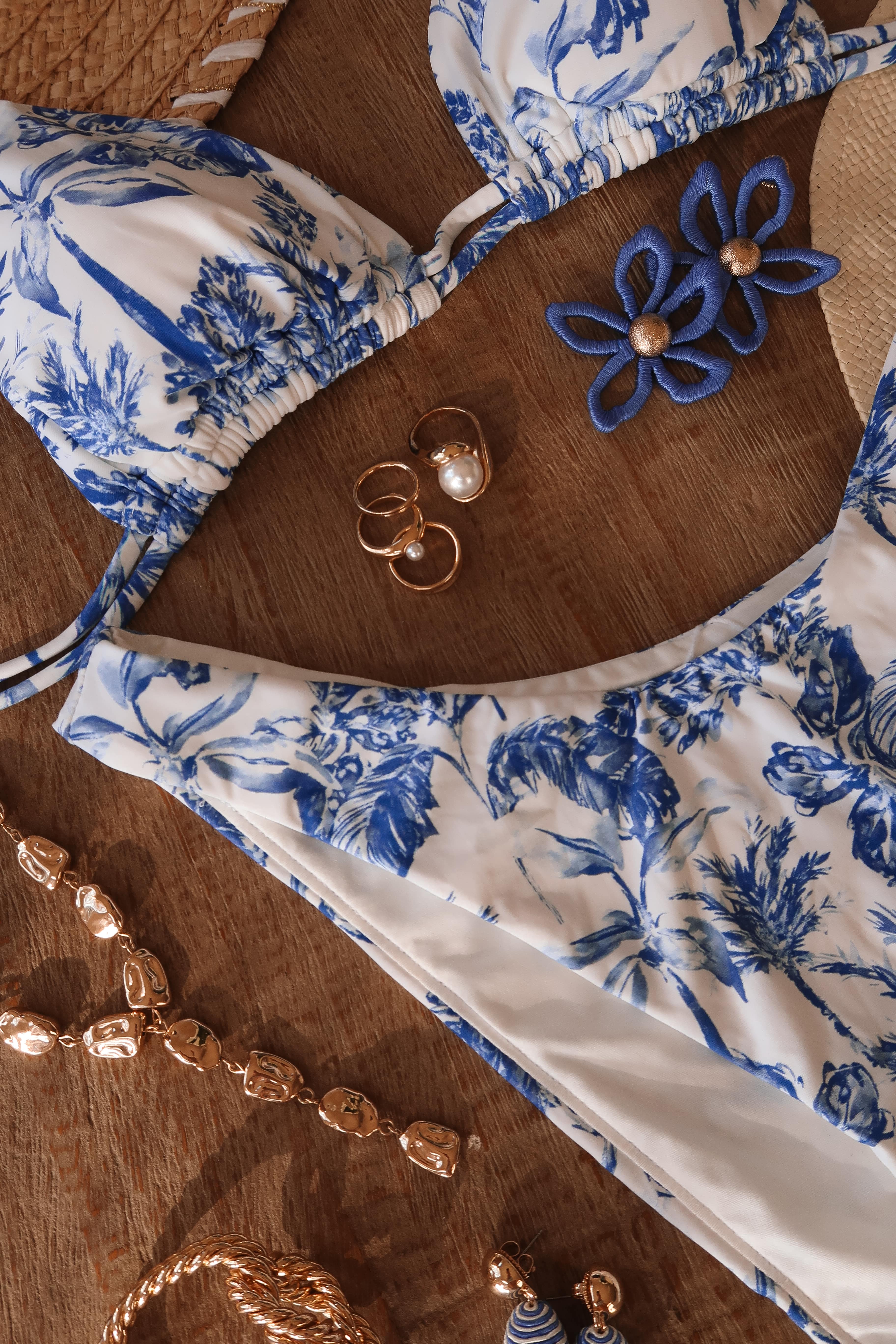 Bikini azul y blanco con estampado de palmeras, complementado con joyas doradas, parte de la colección Shea Leigh Mills para Gianni Bini.