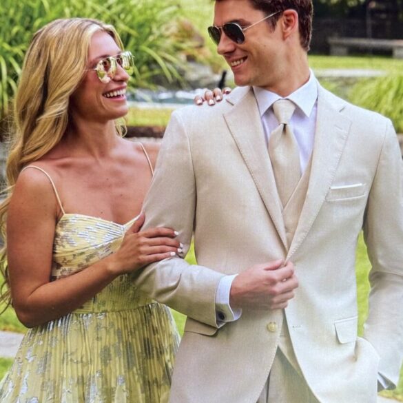 Hombre con traje de prom blanco y lentes de sol junto a mujer, listos para su evento