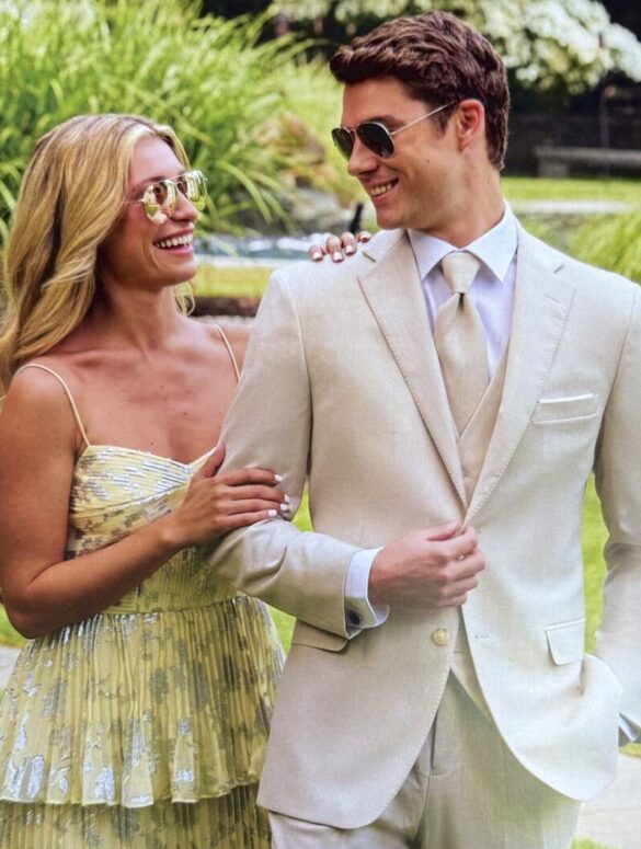 Hombre con traje de prom blanco y lentes de sol junto a mujer, listos para su evento