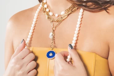 Woman wearing various necklaces of pearl and gold materials.
