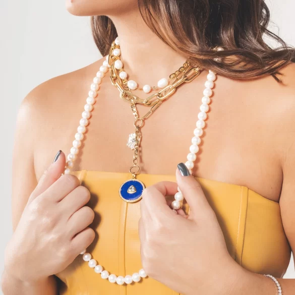 Woman wearing various necklaces of pearl and gold materials.
