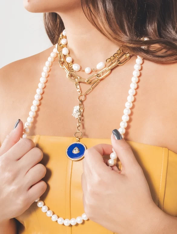 Woman wearing various necklaces of pearl and gold materials.