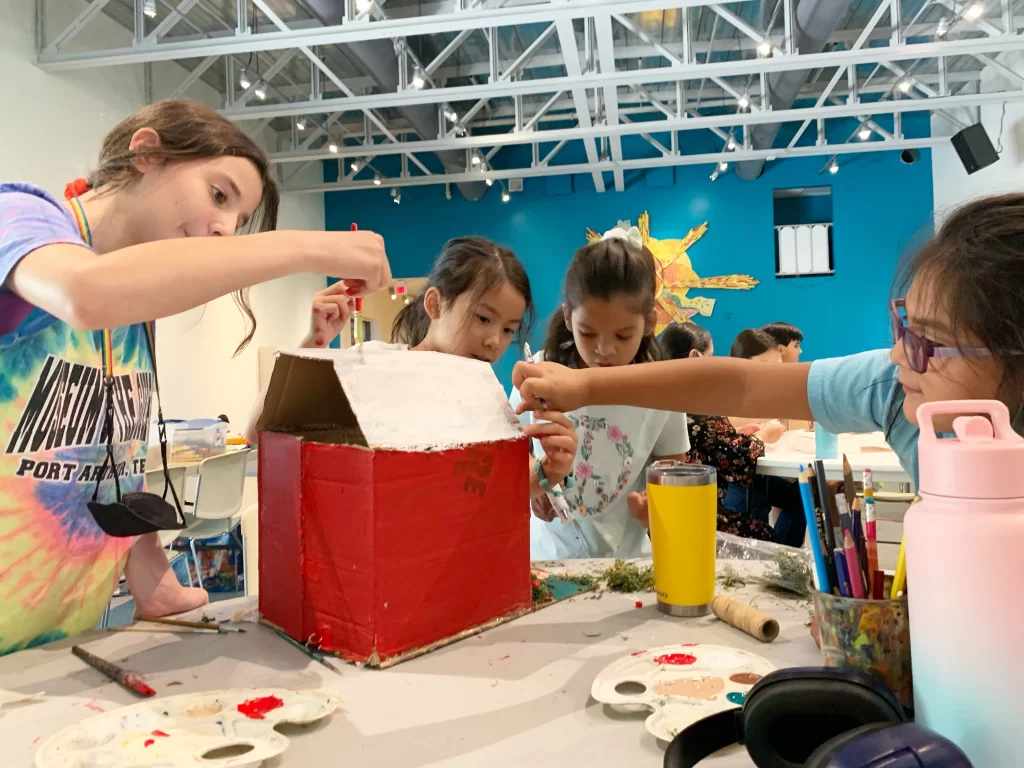 Niñas pintando una casa de cartón en actividad artística en IMAS