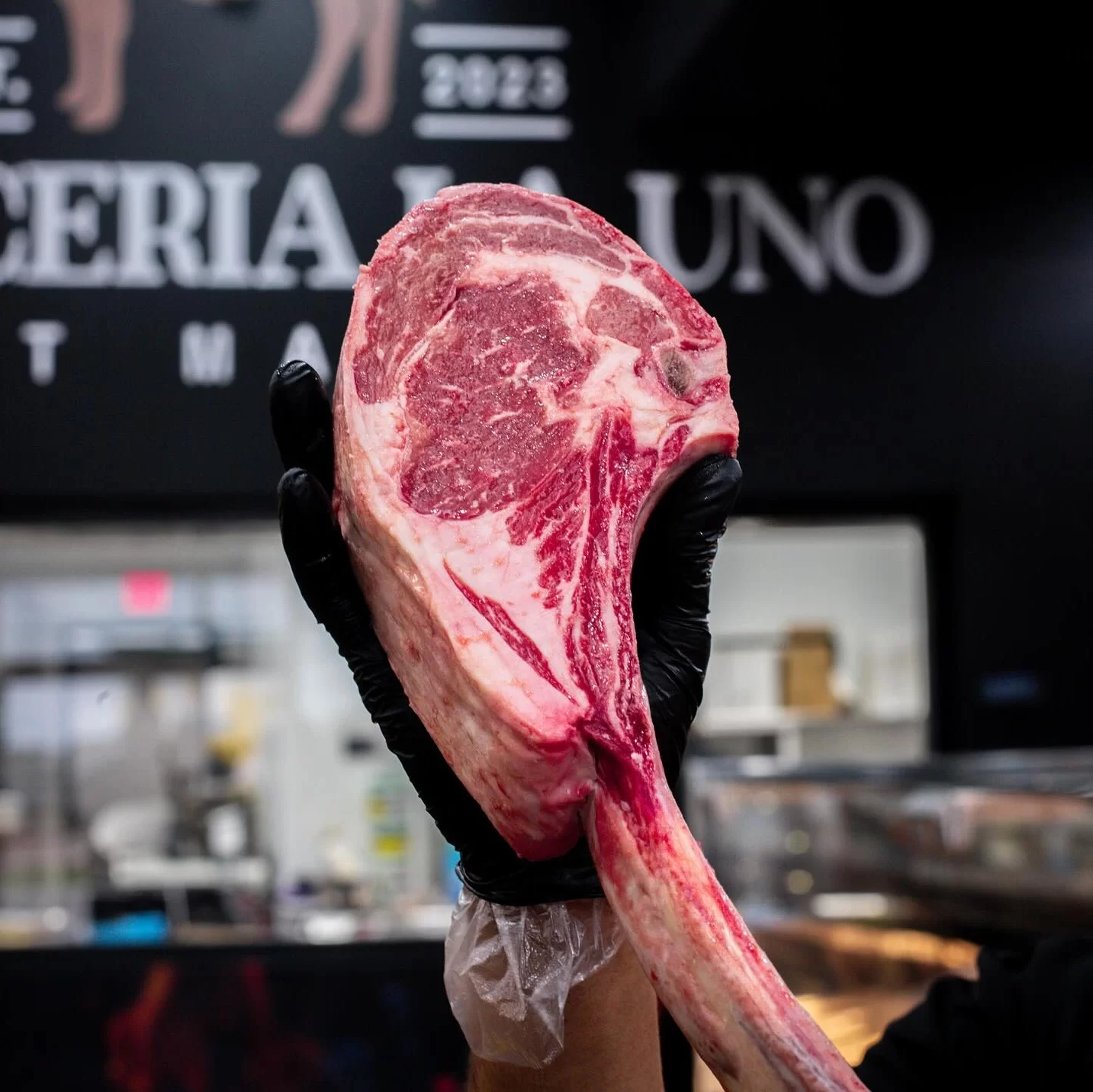 Tomahawk crudo sostenido con guante negro en Carnicería La Uno, Edinburg